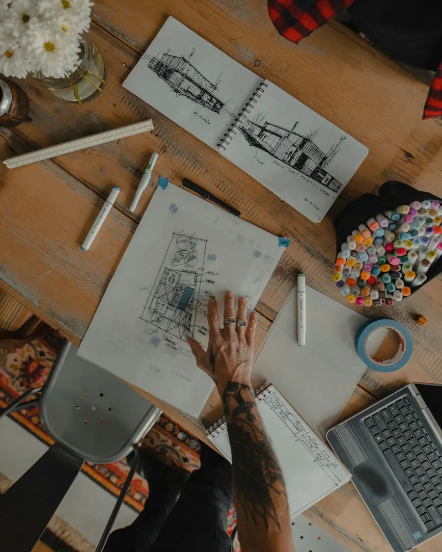 Sketsa dan alat gambar berserakan di meja kayu